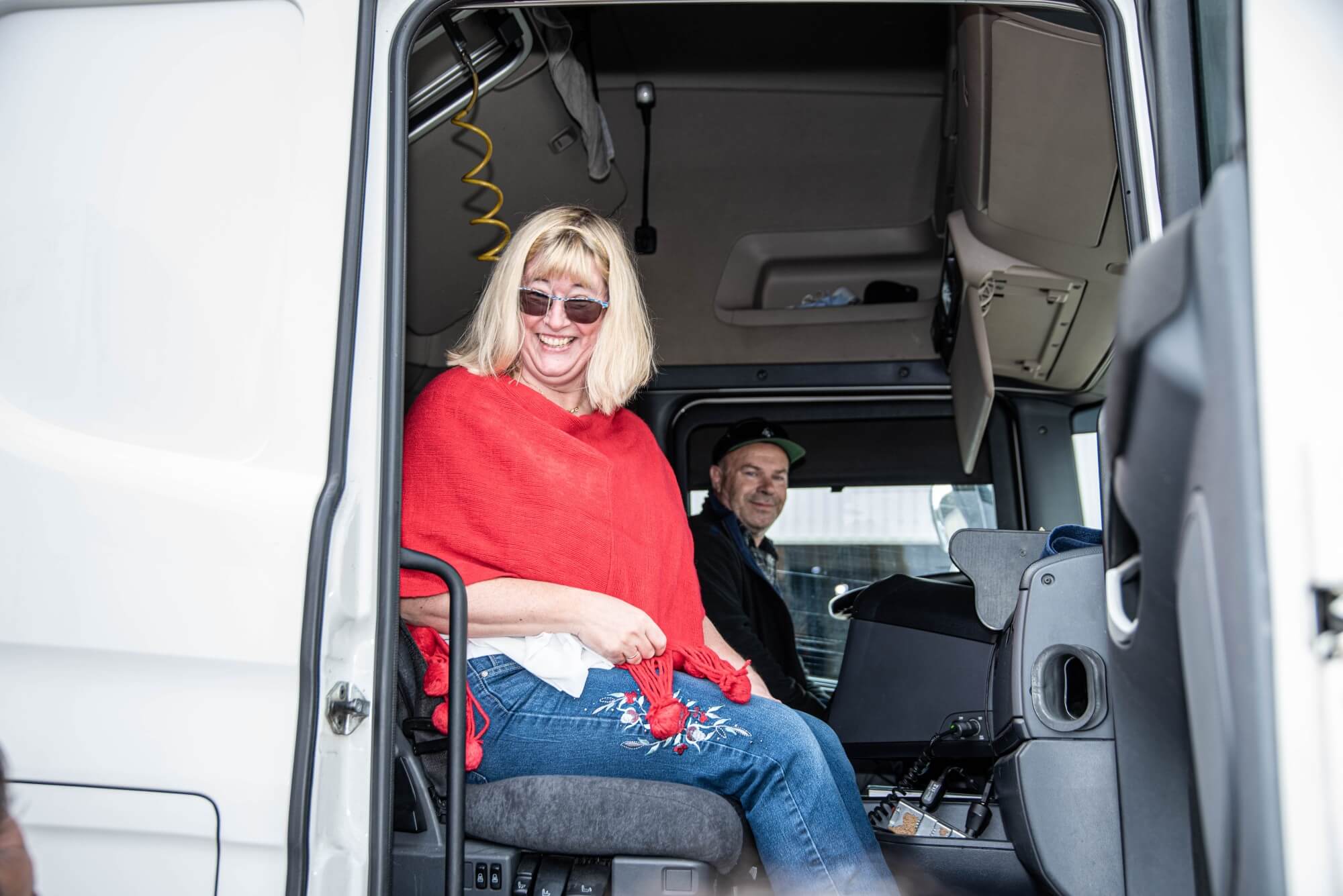Künstlerin Brigitte Riedel sitzt im Beifahrersitz vom LKW bei offener Türe. Hinter Ihr sitzt der LKW-Fahrer.